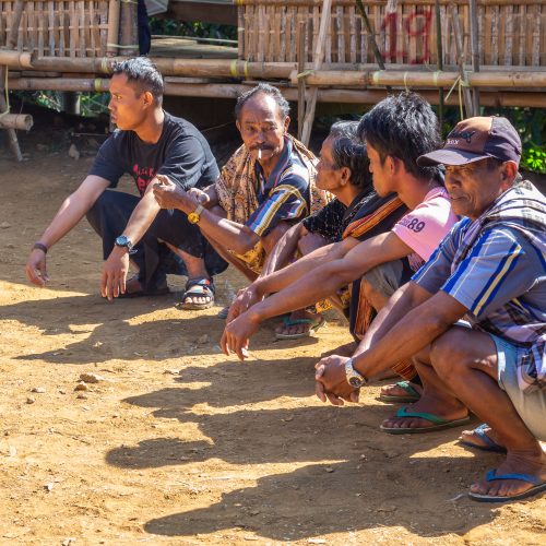 Sulawesi Island, Indonesia - August, 15 2015: Men sitting on haunches and talking in village